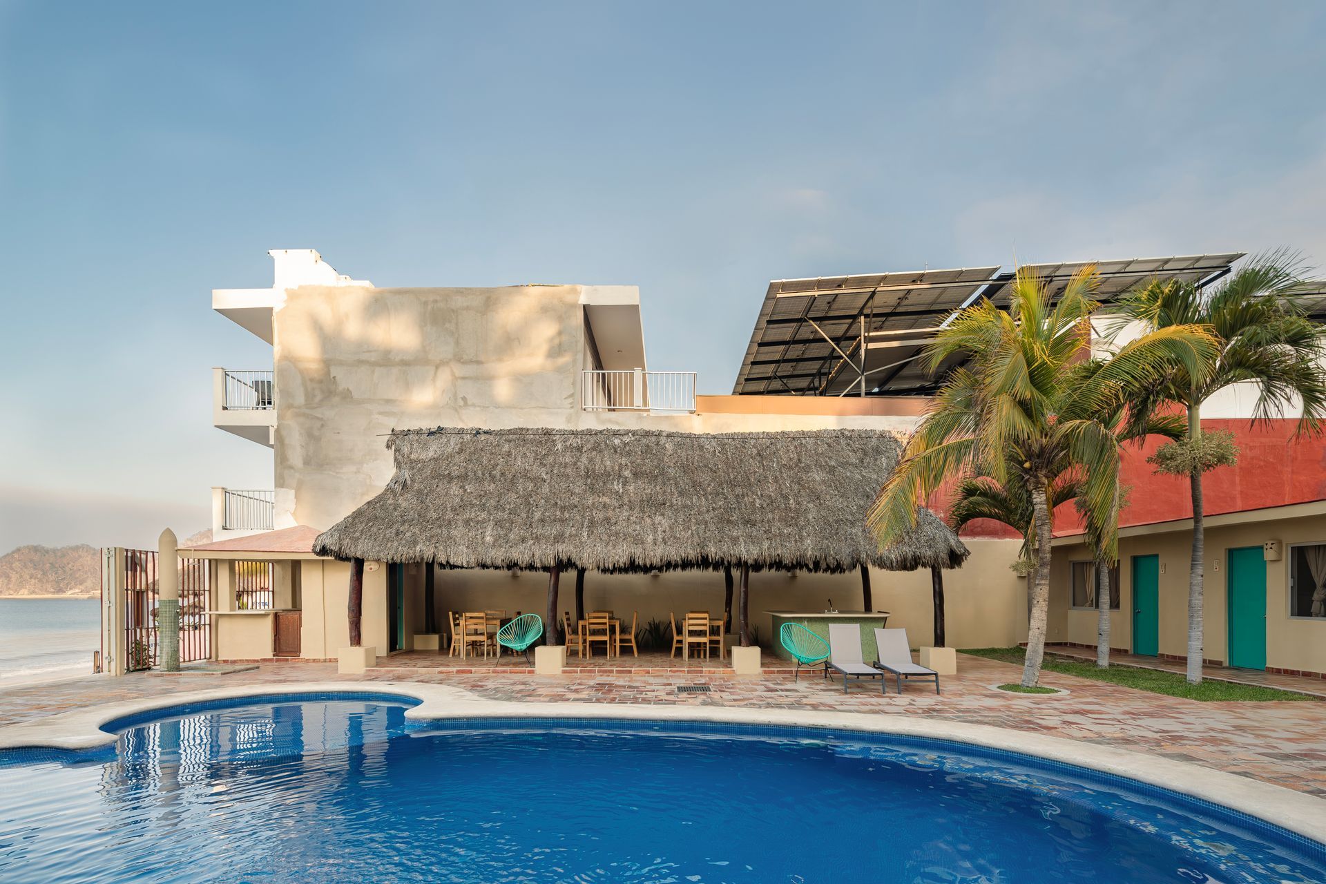 A large swimming pool in front of a building with a thatched roof.
