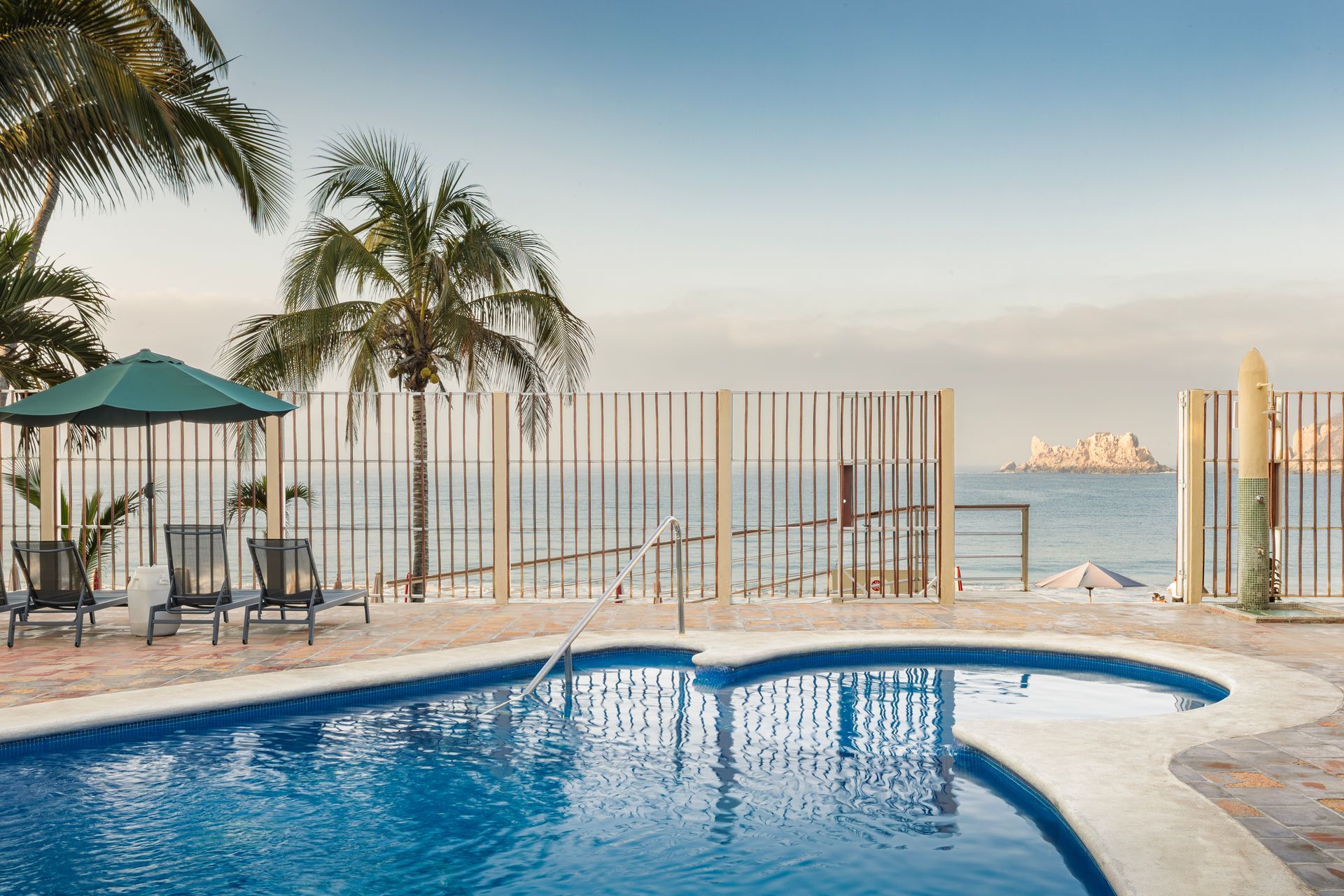 A large swimming pool surrounded by palm trees and chairs next to the ocean.