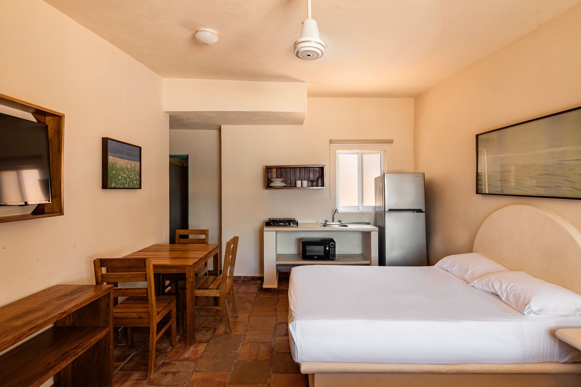 A hotel room with a bed , table , chairs and refrigerator.