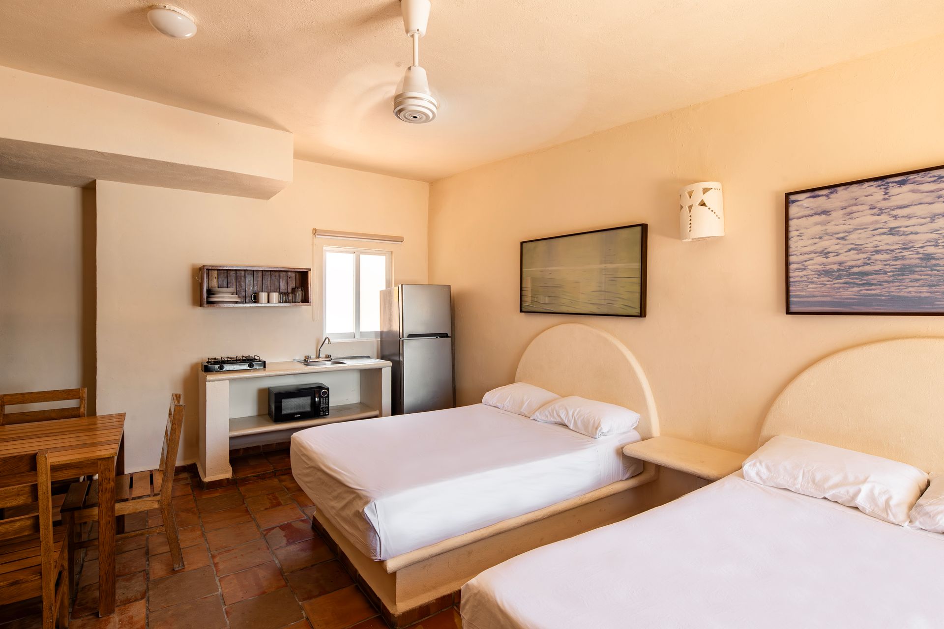 A hotel room with two beds , a refrigerator , a table and chairs.