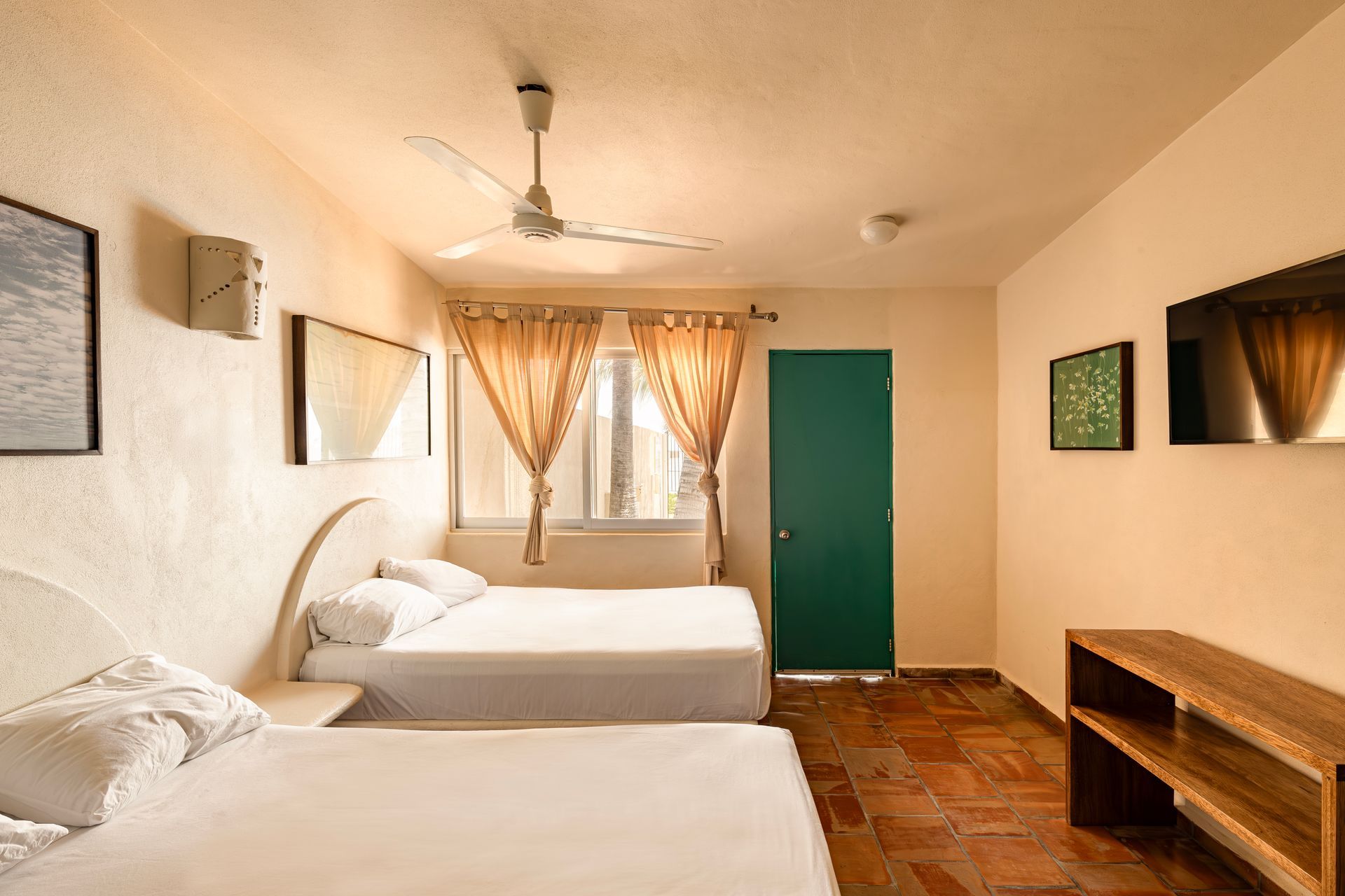 A hotel room with two beds , a ceiling fan and a green door.