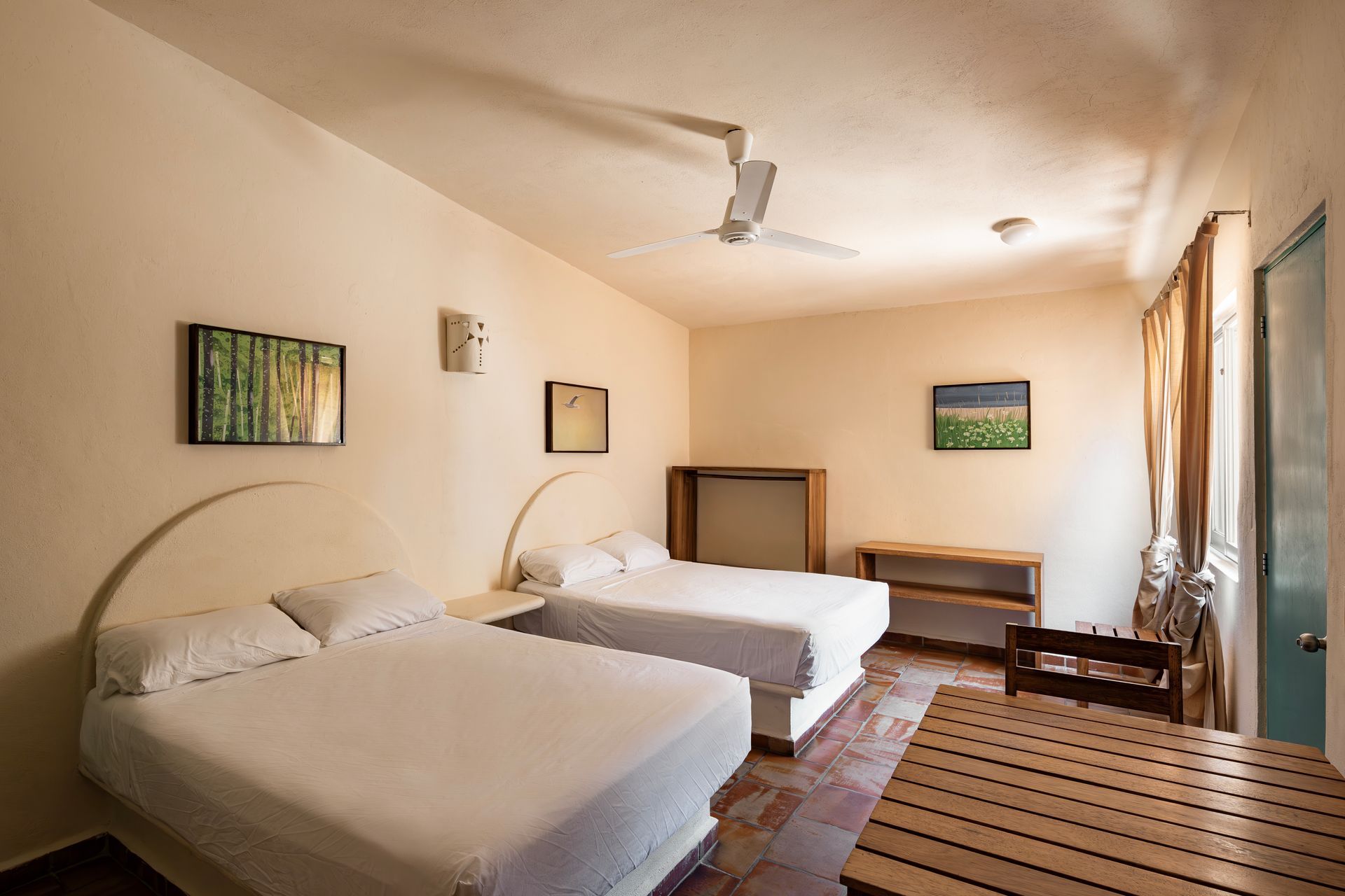 A hotel room with two beds , a table and a ceiling fan.