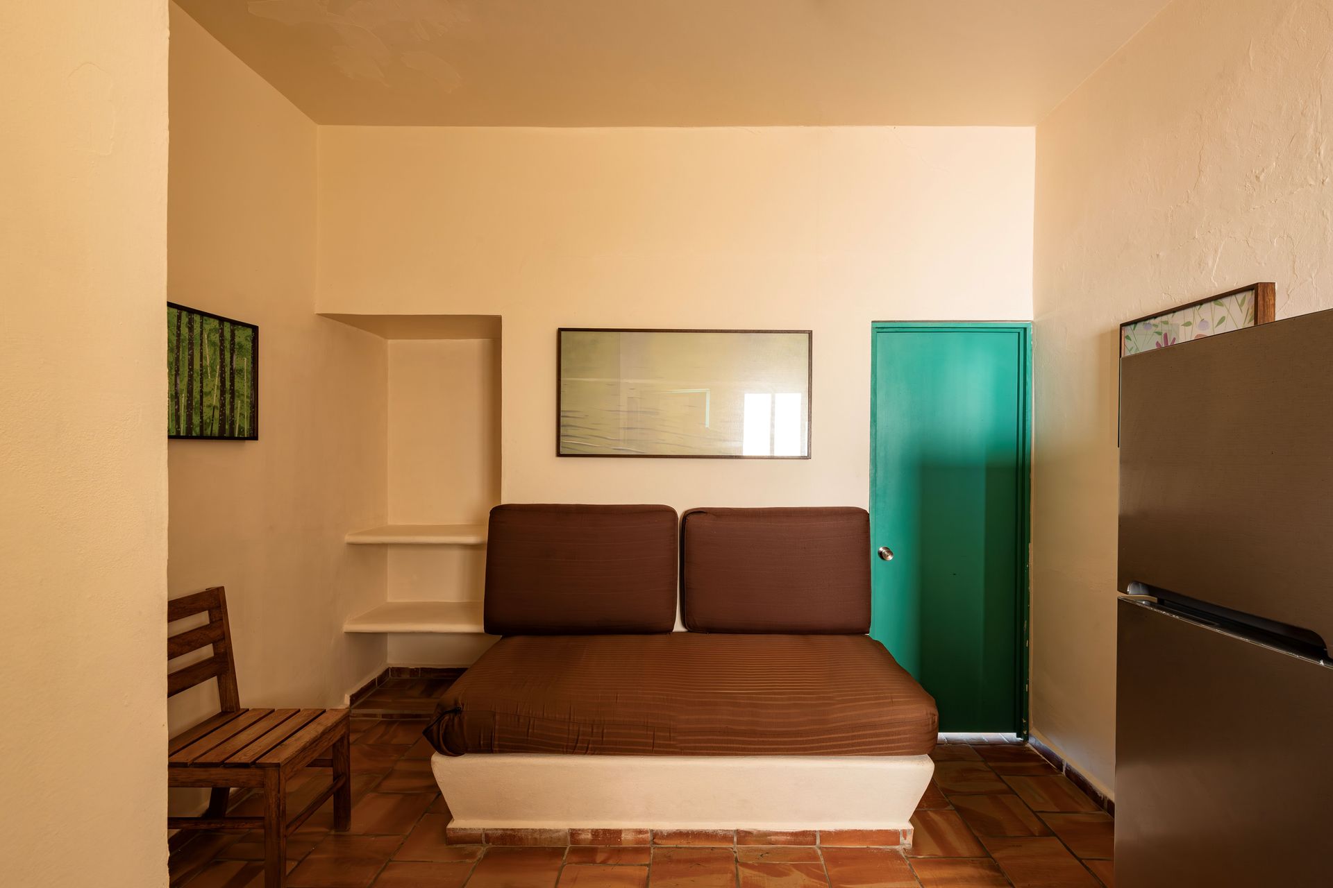 A room with a couch , chair , refrigerator and a green door.