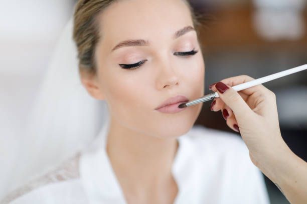 A woman is getting her lips painted by a makeup artist.