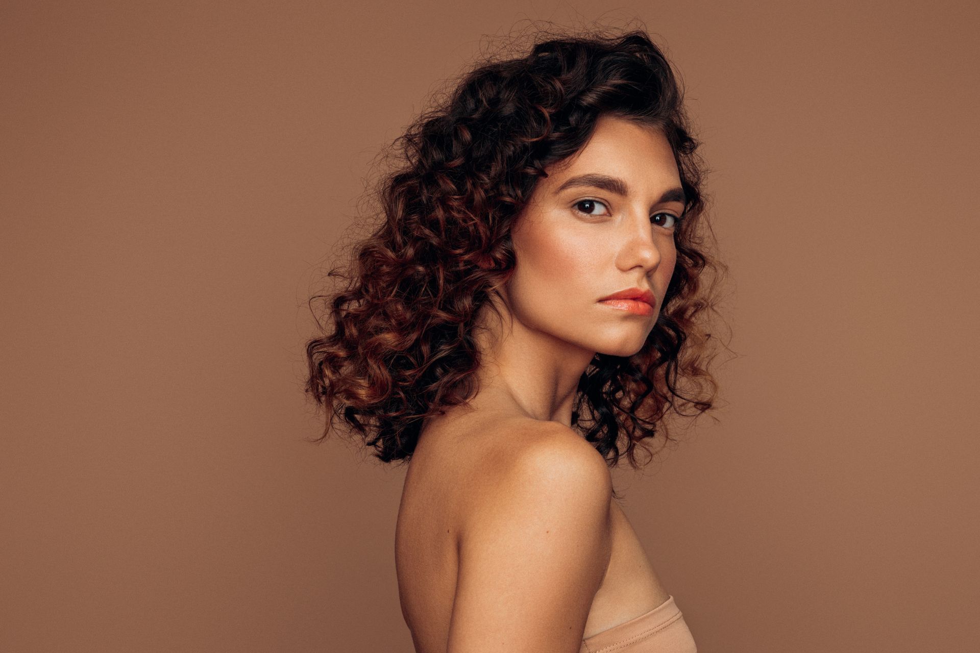 A woman with curly hair is looking over her shoulder at the camera.