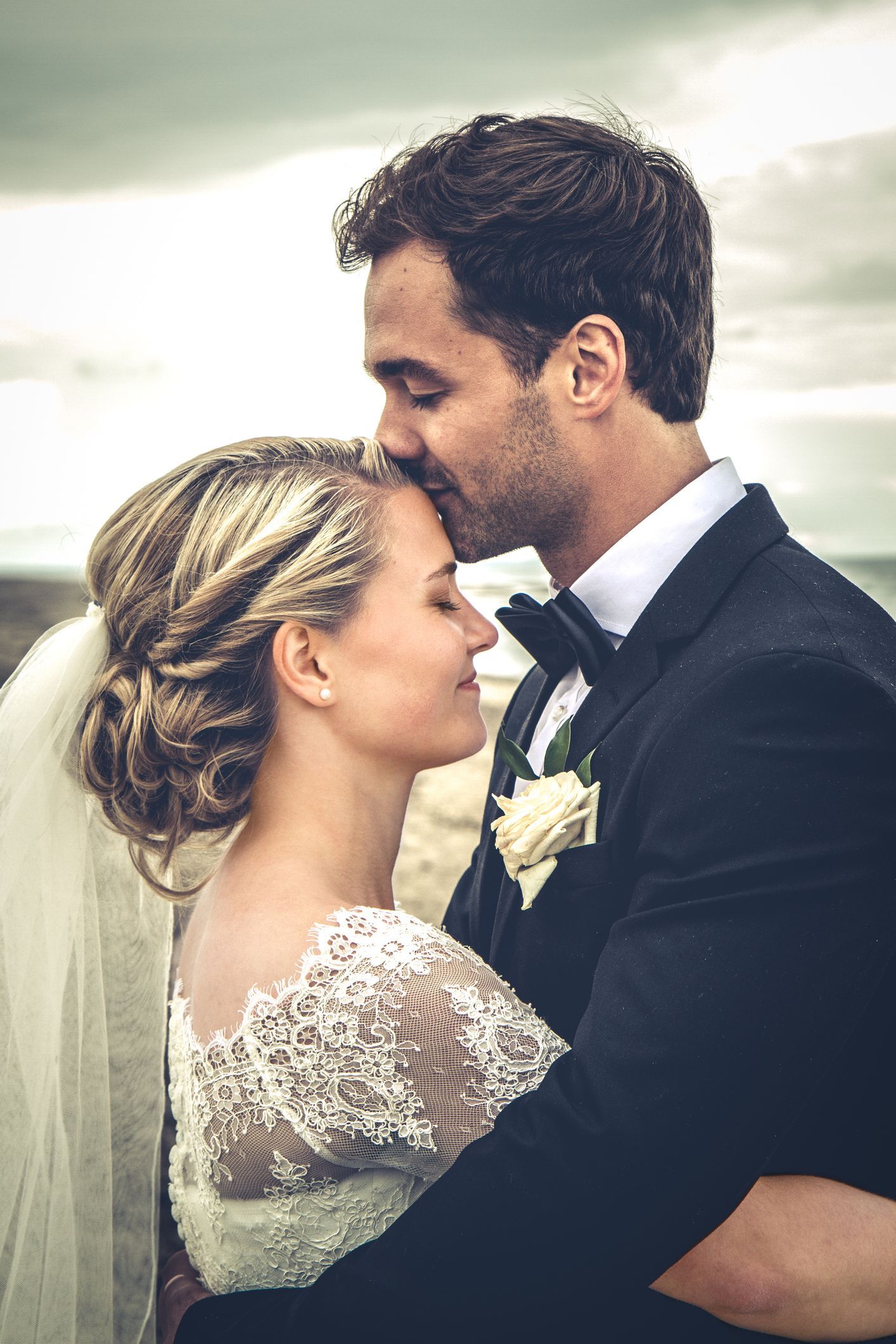 A bride and groom are kissing in the rain on their wedding day.