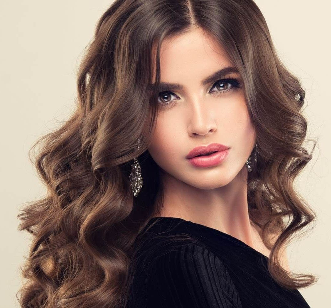 A woman with long curly hair is wearing a black top and earrings.