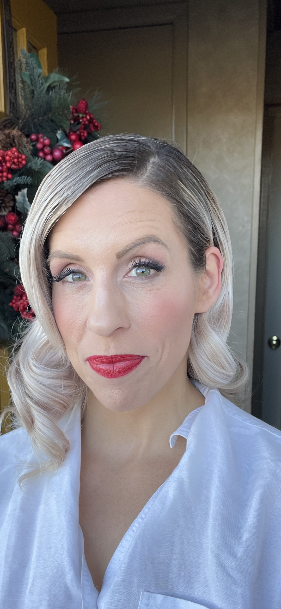 A Woman with Blonde Hair and Red Lipstick Is Standing in Front of A Christmas Tree.