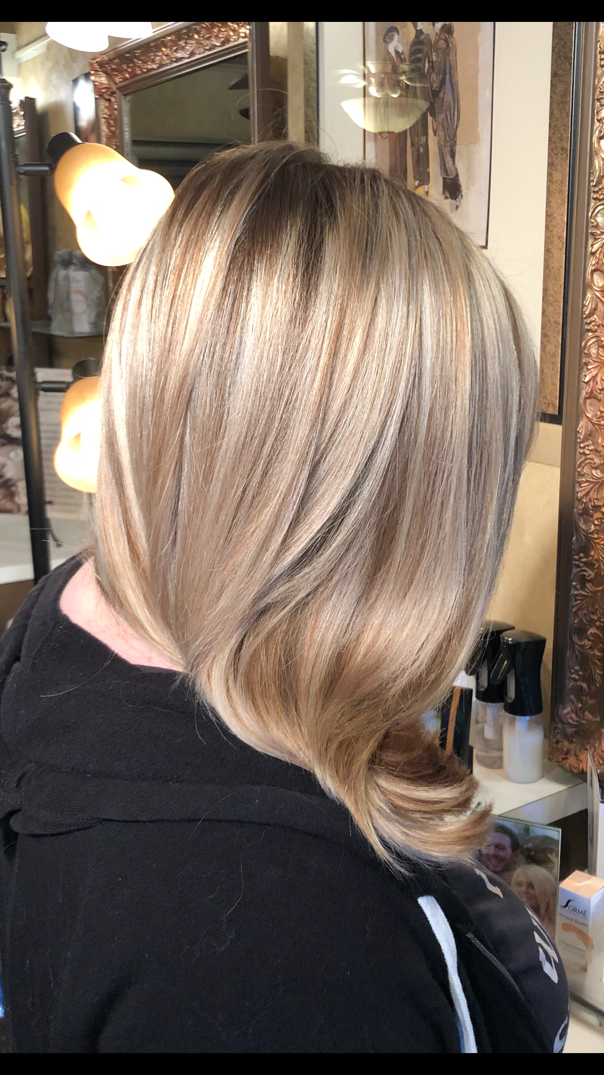 A woman with blonde hair is sitting in front of a mirror in a salon.