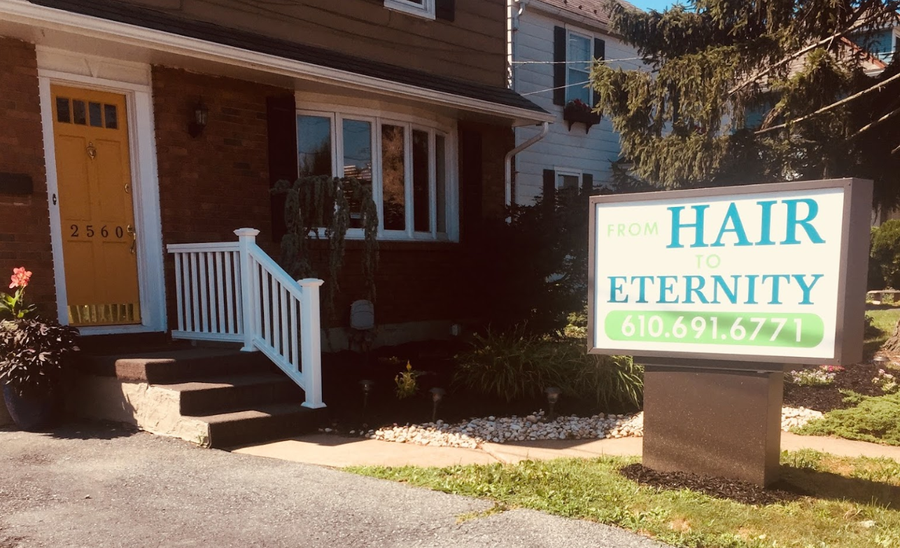 A sign for a hair salon is in front of a house.