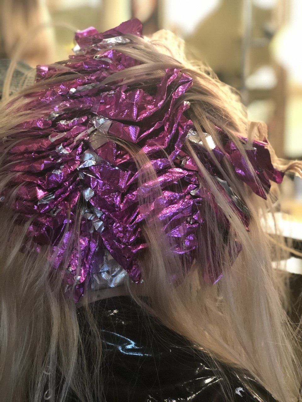 A woman is getting her hair dyed with purple foil.