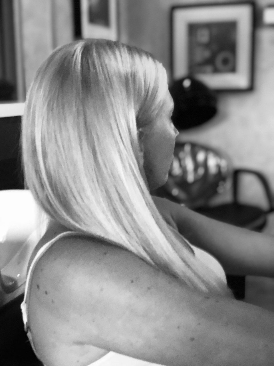 A woman with long blonde hair is sitting in a chair in a black and white photo.