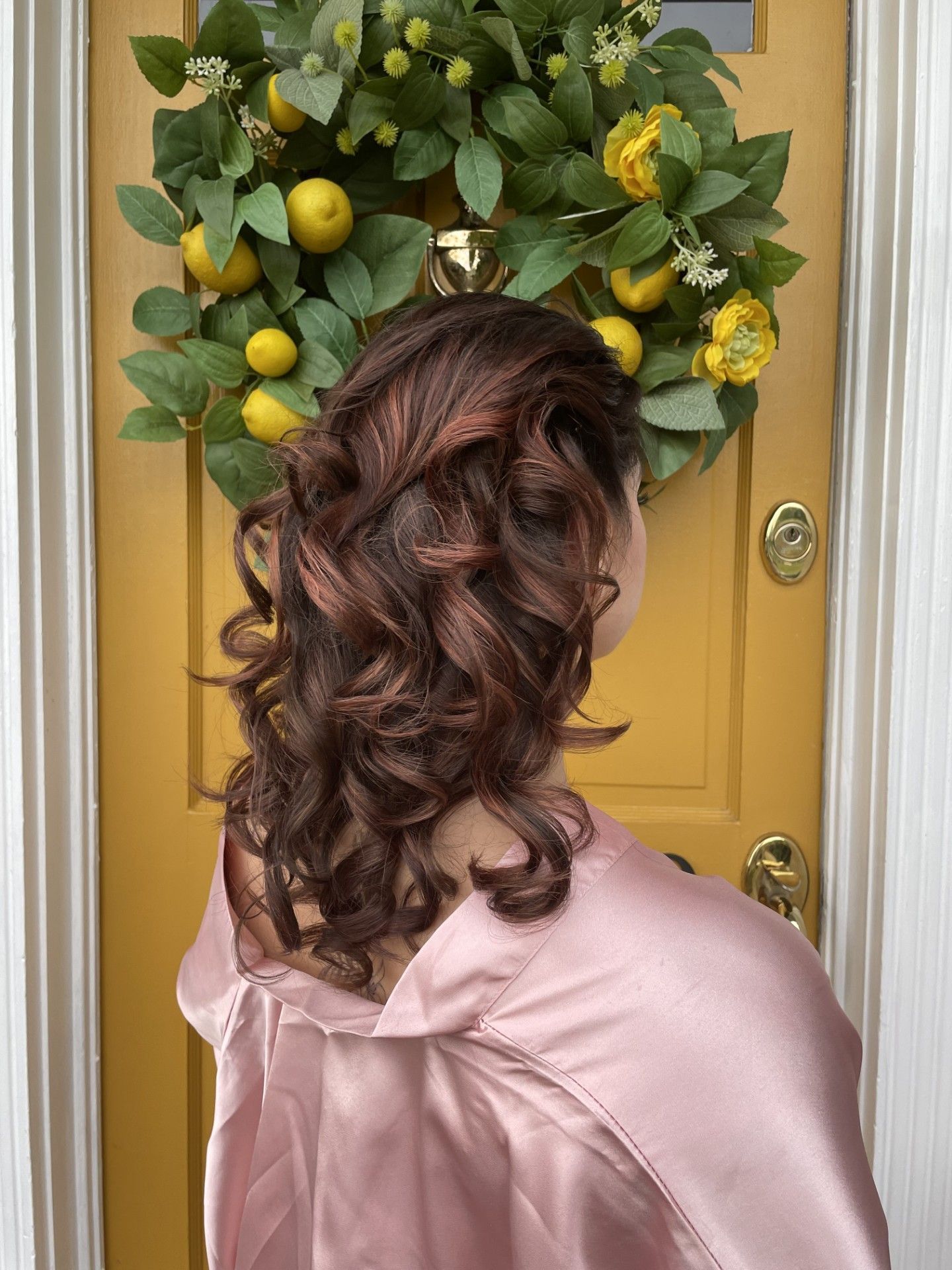 A woman in a pink robe is standing in front of a yellow door with a wreath of lemons on it.
