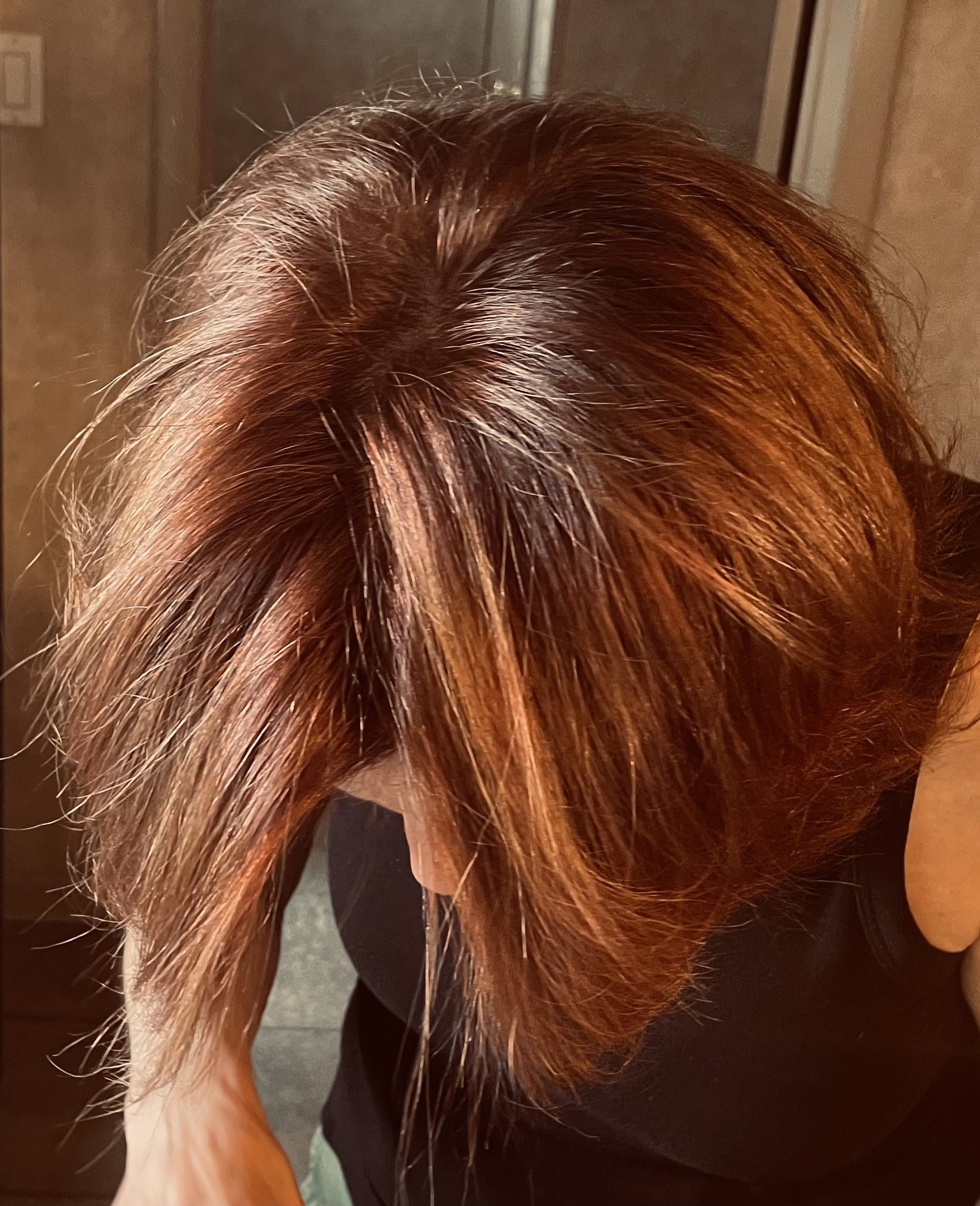 A woman is looking down at her hair in front of a mirror.