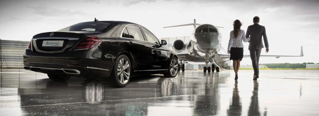 A man and a woman are walking towards a car and an airplane.