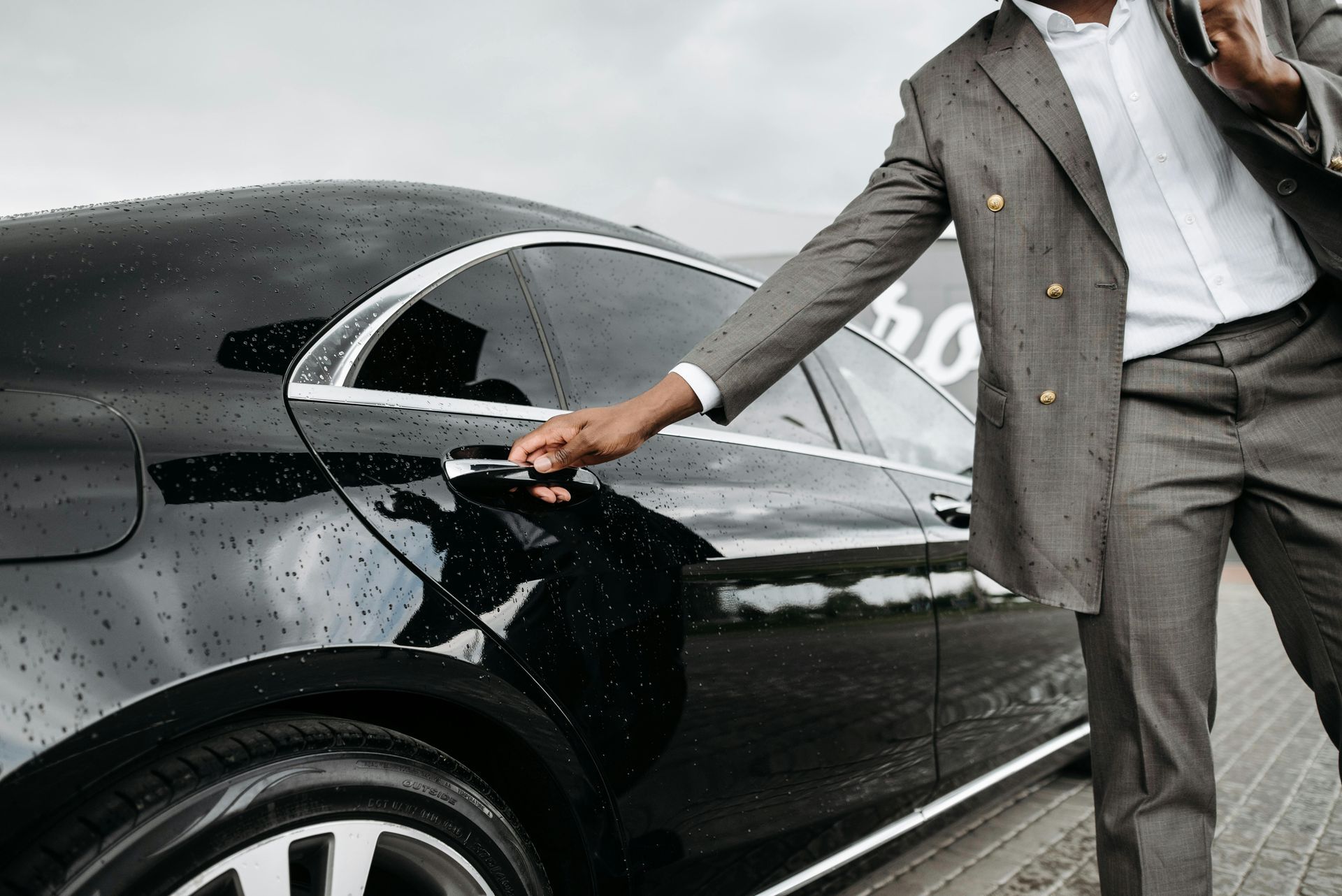 A man in a suit is standing next to a black car and talking on a cell phone.