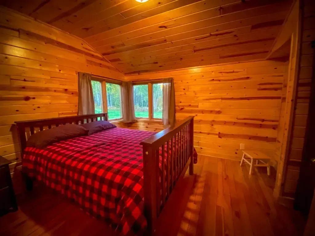 A bedroom in a log cabin with a bed and two windows.