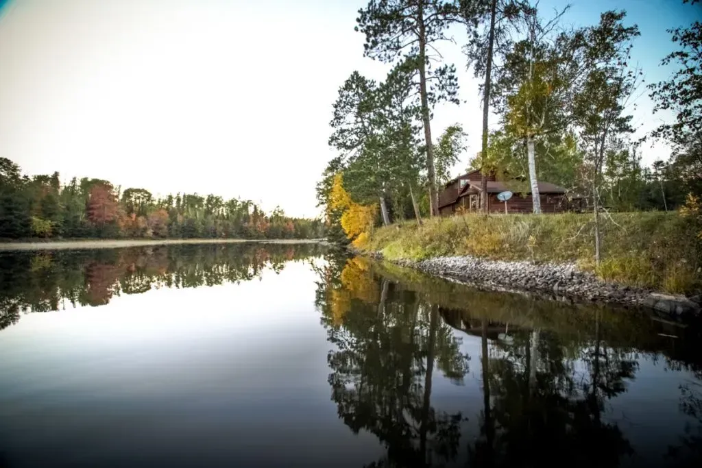 A house sits on a small island in the middle of a lake surrounded by trees.