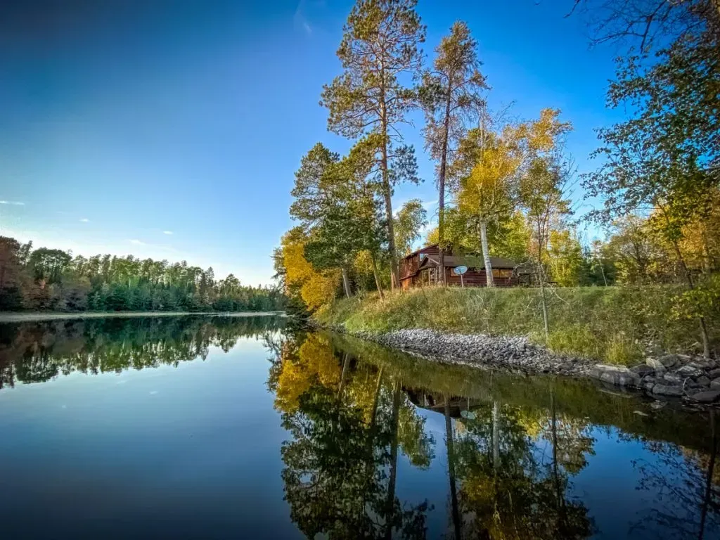 A house is sitting on the shore of a lake surrounded by trees.