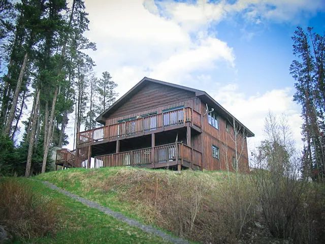 A large wooden house is sitting on top of a hill surrounded by trees.