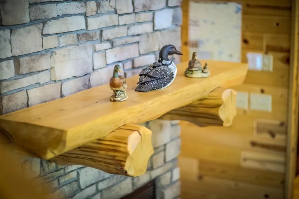 A wooden shelf with a duck on top of it next to a fireplace.