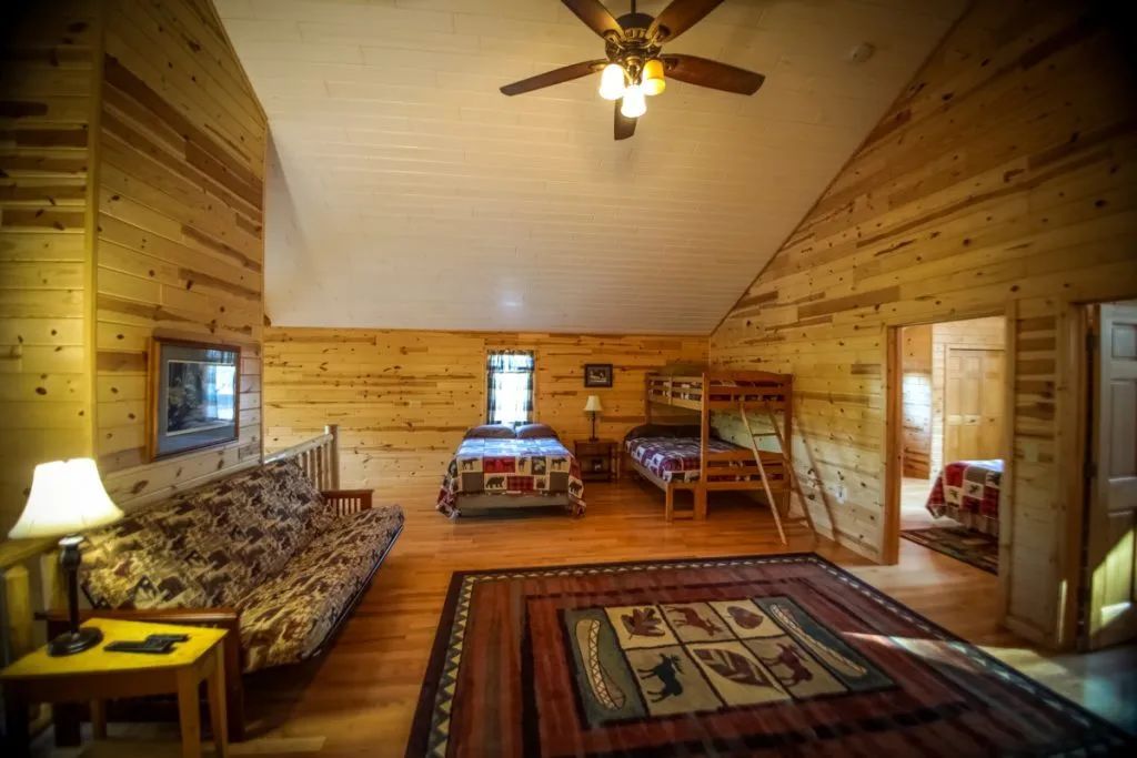 A large wooden cabin with a futon , two beds , and a ceiling fan.