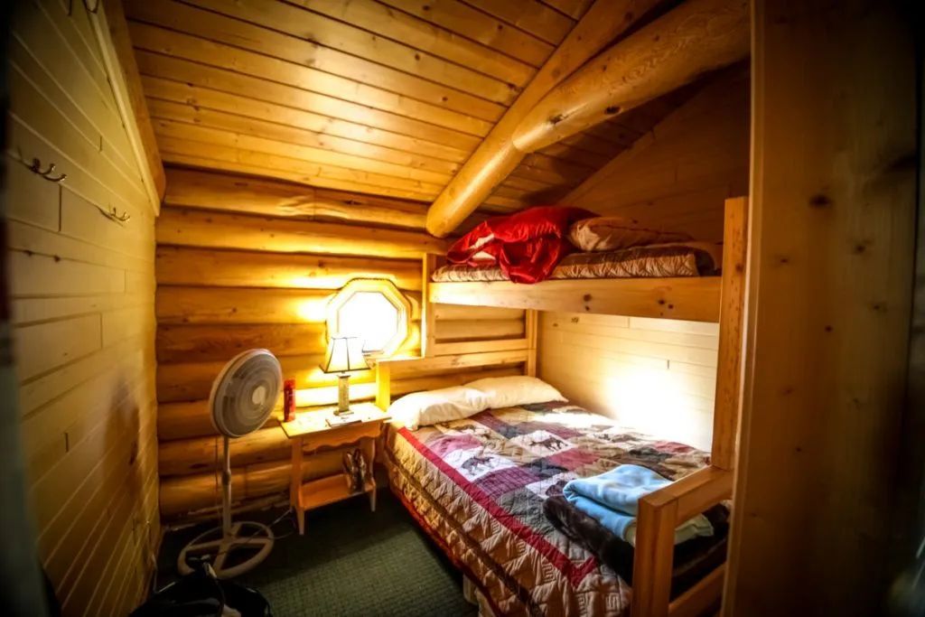 A bedroom in a log cabin with bunk beds and a fan.