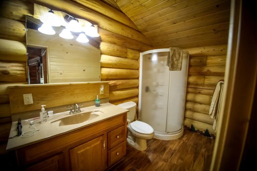 A bathroom in a log cabin with a sink , toilet and shower.