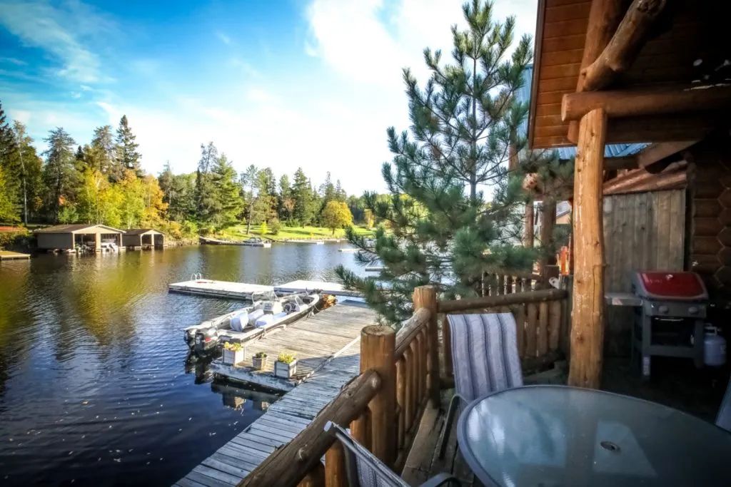 There is a table and chairs on the balcony overlooking a lake.