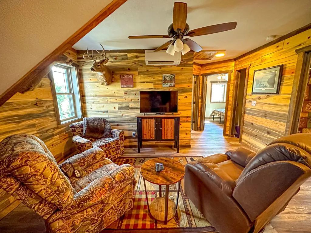 A living room in a log cabin with a couch , chairs , table and television.