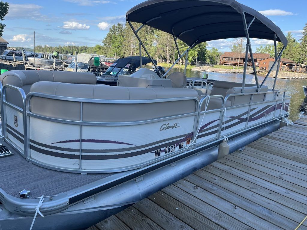 A pontoon boat with a canopy is docked at a dock.