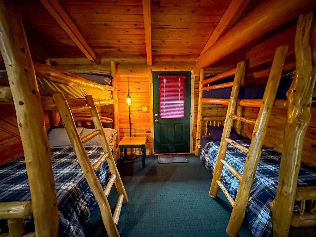 A room in a log cabin with bunk beds and a door.