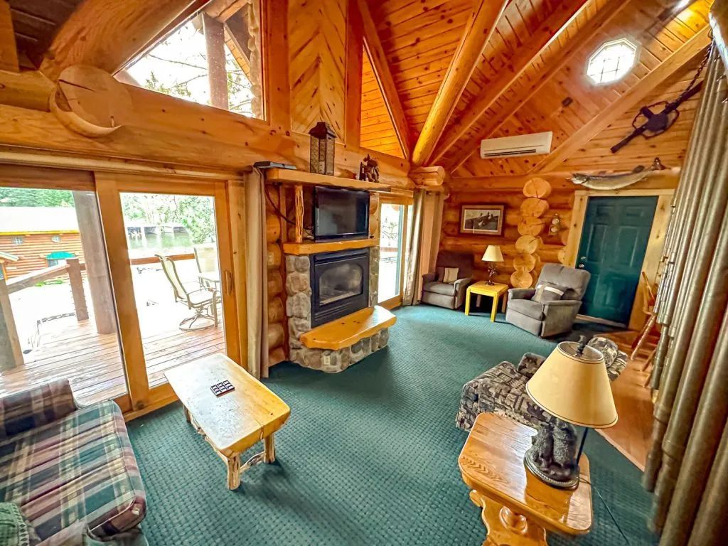 A living room in a log cabin with a fireplace and lots of windows.