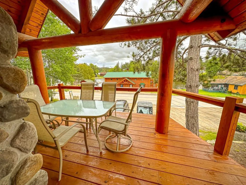 There is a table and chairs on the deck of a log cabin.