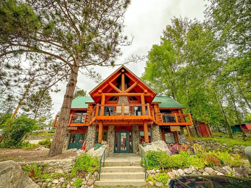 A large log cabin with a green roof is surrounded by trees.