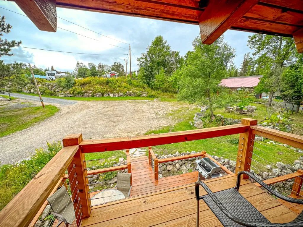 A wooden deck with a chair on it and a view of a dirt road.