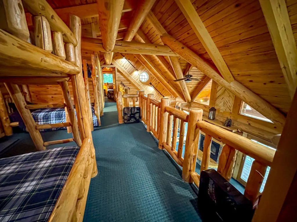 A hallway in a log cabin with bunk beds and a railing.