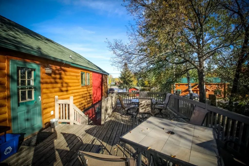 A wooden deck with a table and chairs in front of a log cabin.