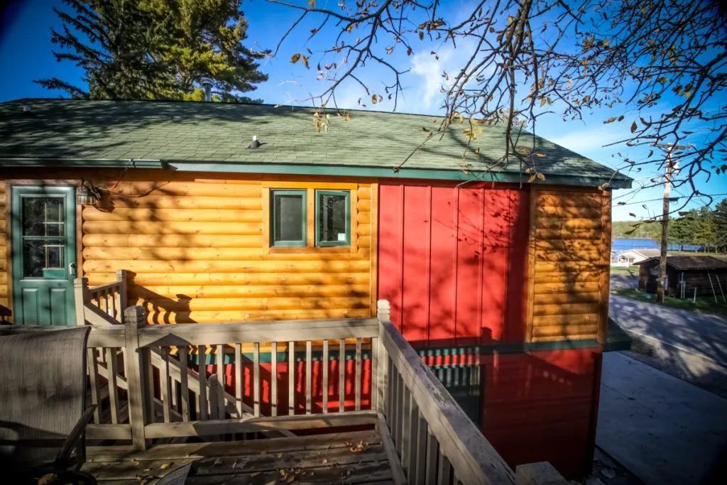 A wooden house with a red door and a wooden deck.