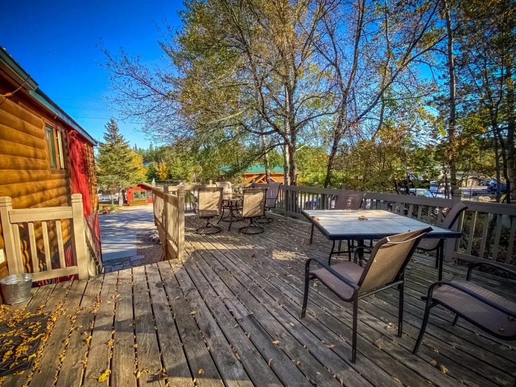 A wooden deck with tables and chairs in front of a log cabin.