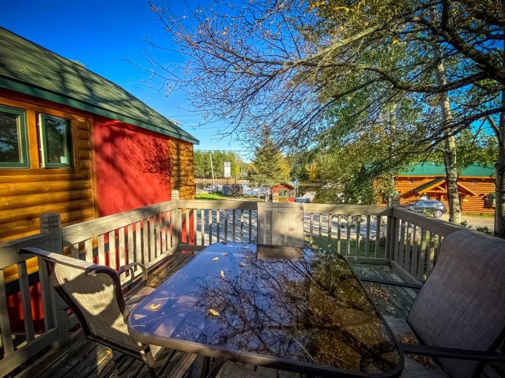 There is a table and chairs on the deck of a log cabin.