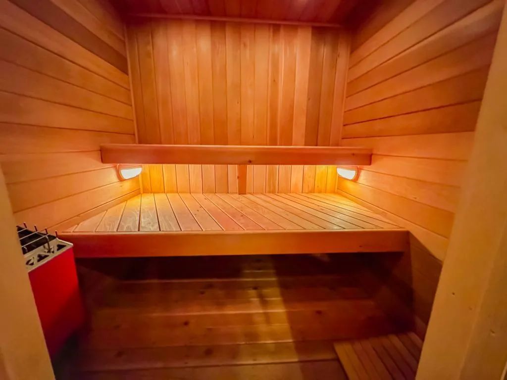 A wooden sauna with a bench and a red heater.