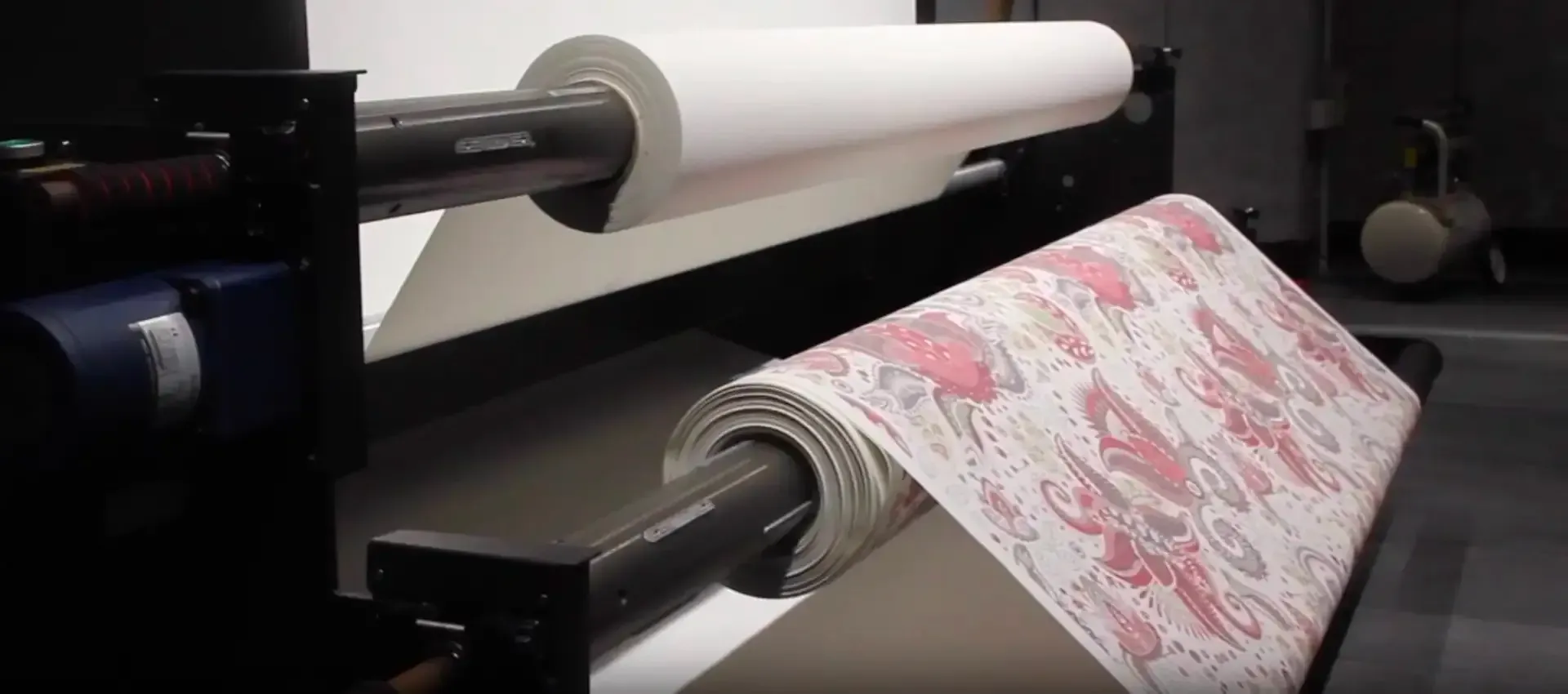 Person screen printing a colorful design on a grey t-shirt in a workshop, wearing a green shirt and apron.