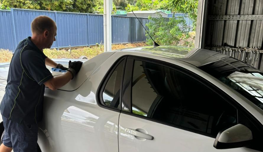 A Man Is Cleaning A White Car In A Garage — SnP Mechanical & Detailing In Murwillumbah, NSW