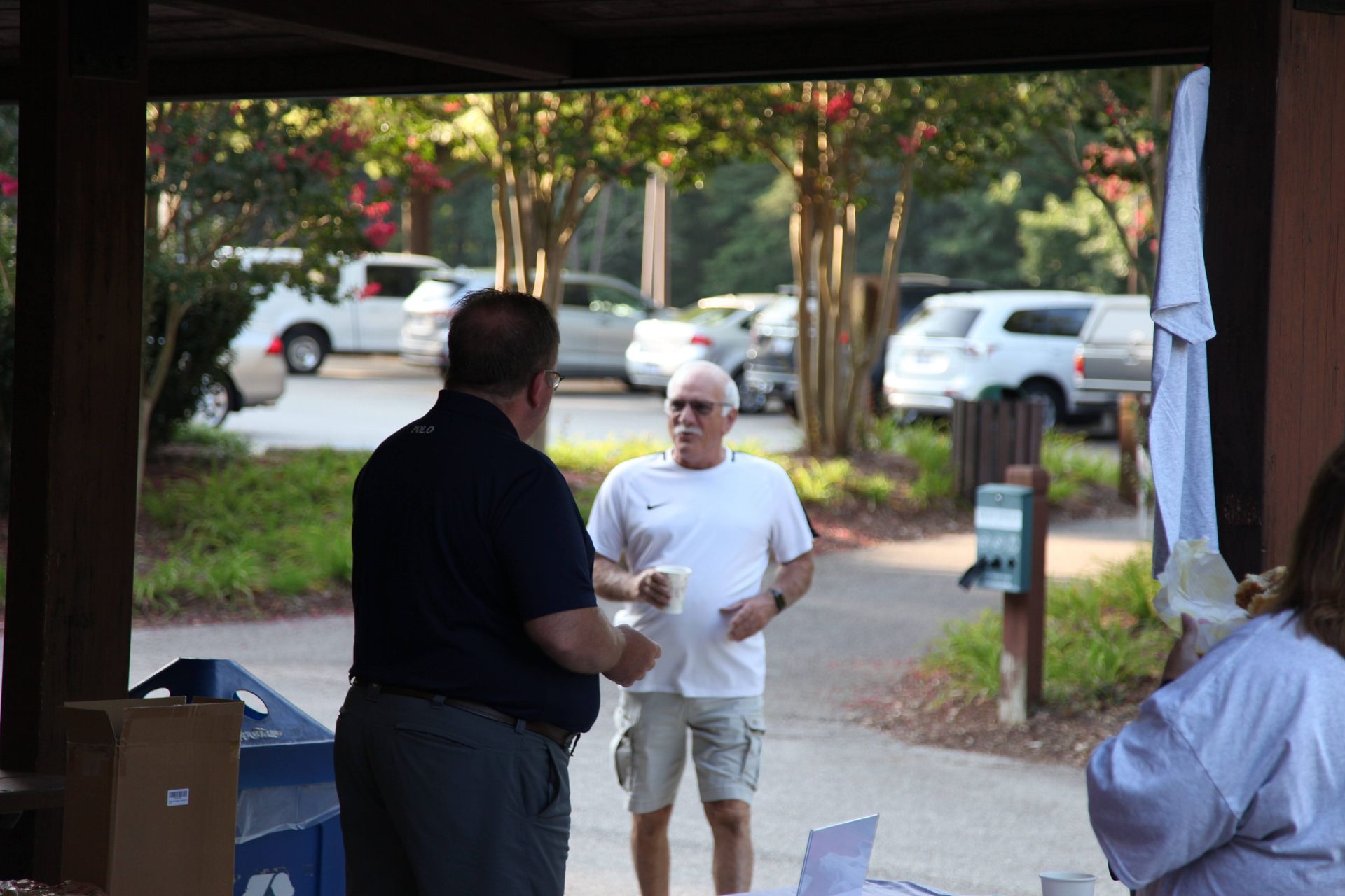 Two men are standing next to each other in a parking lot talking to each other.