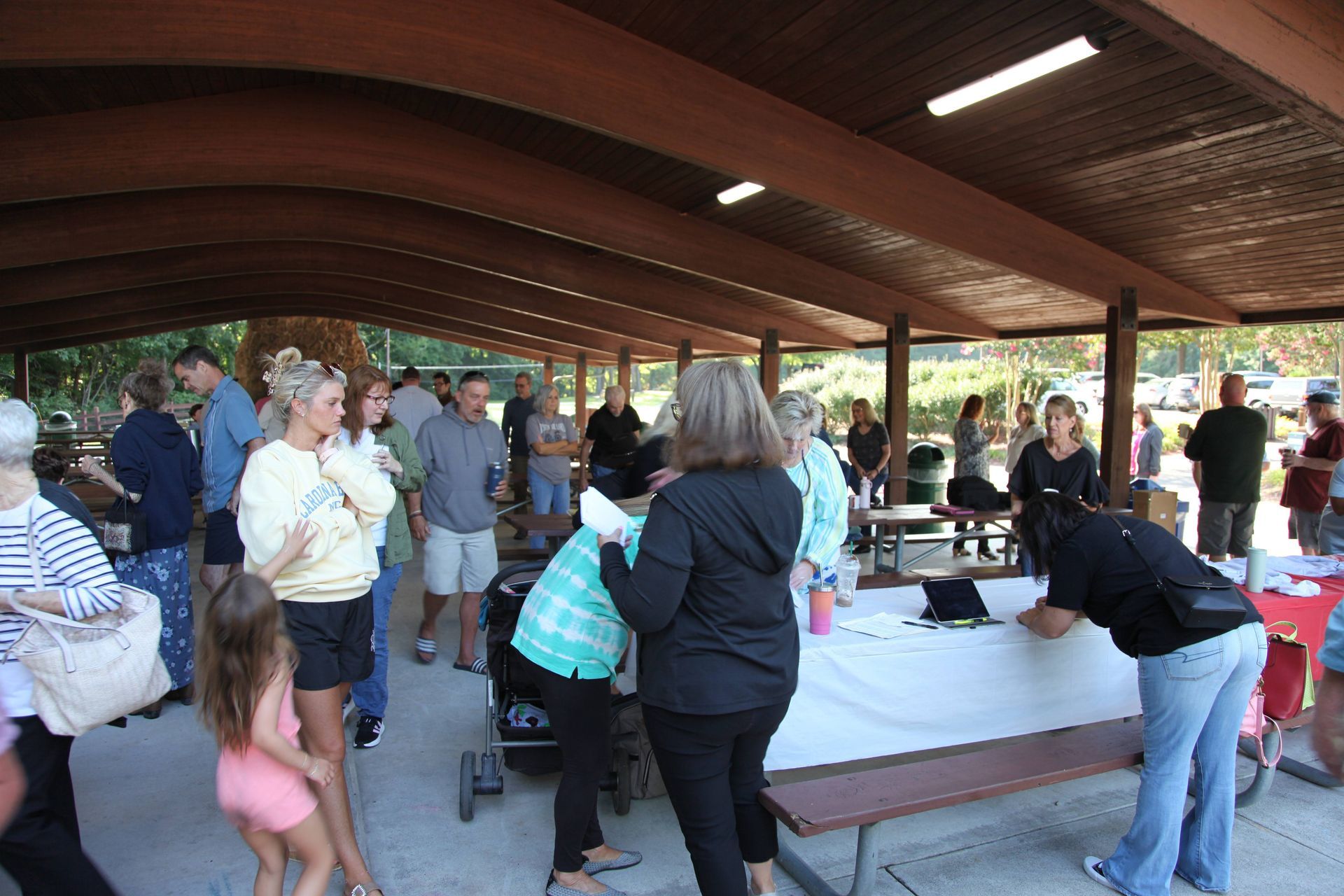 A group of people are standing around a picnic table under a covered area.