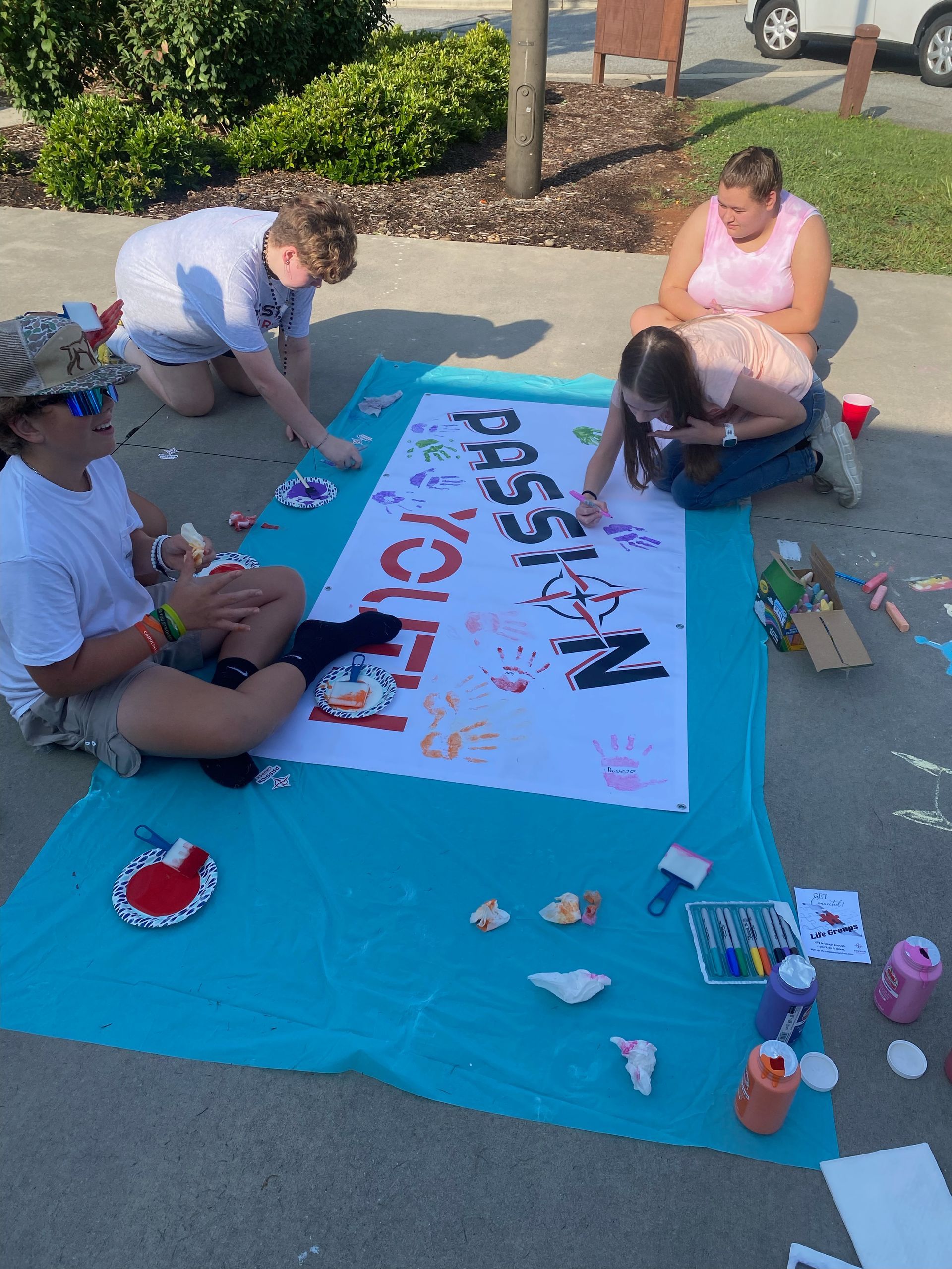 A group of people are sitting on the ground painting a sign that says passion