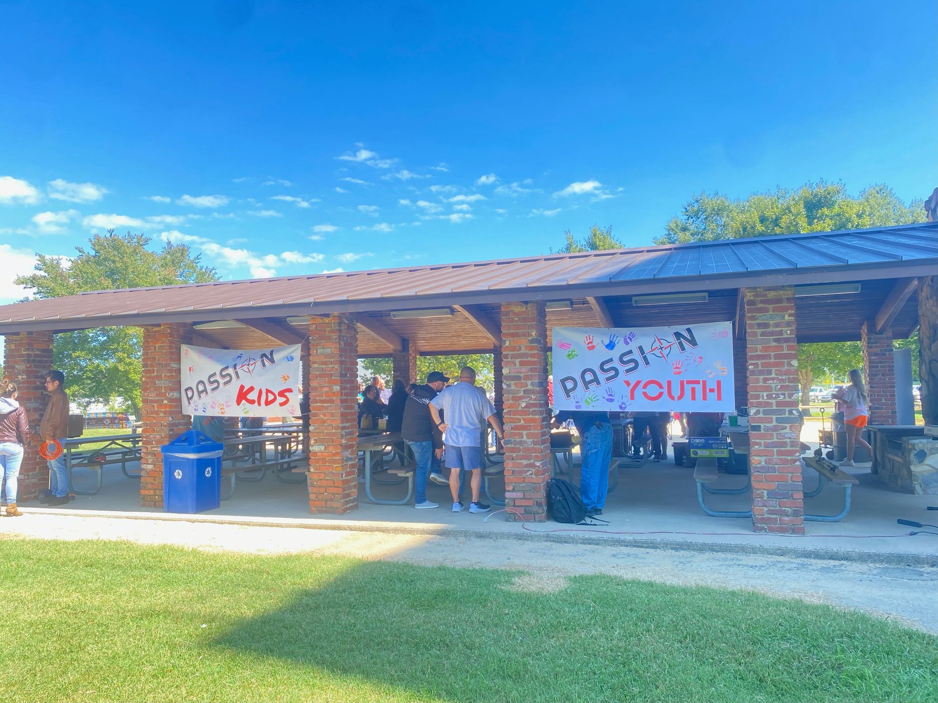 A group of people are standing under a pavilion in a park.