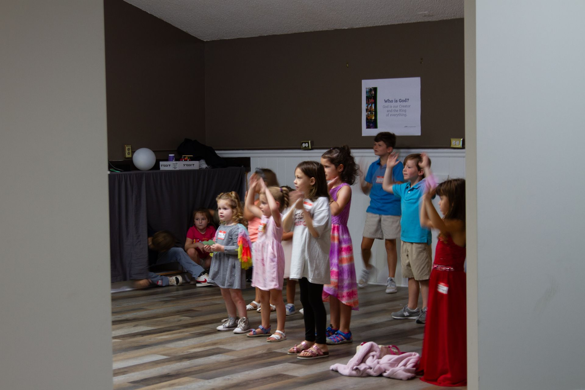 A group of children are standing in a room clapping their hands.