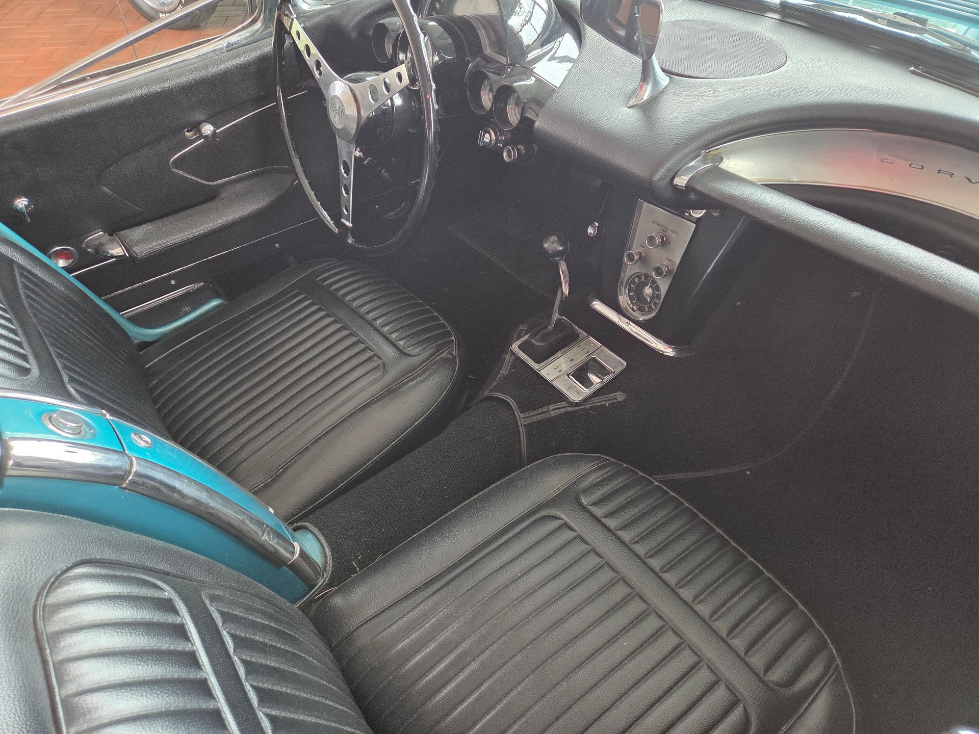 Interior of a vintage car with black leather seats and turquoise trim, viewed from the passenger side.